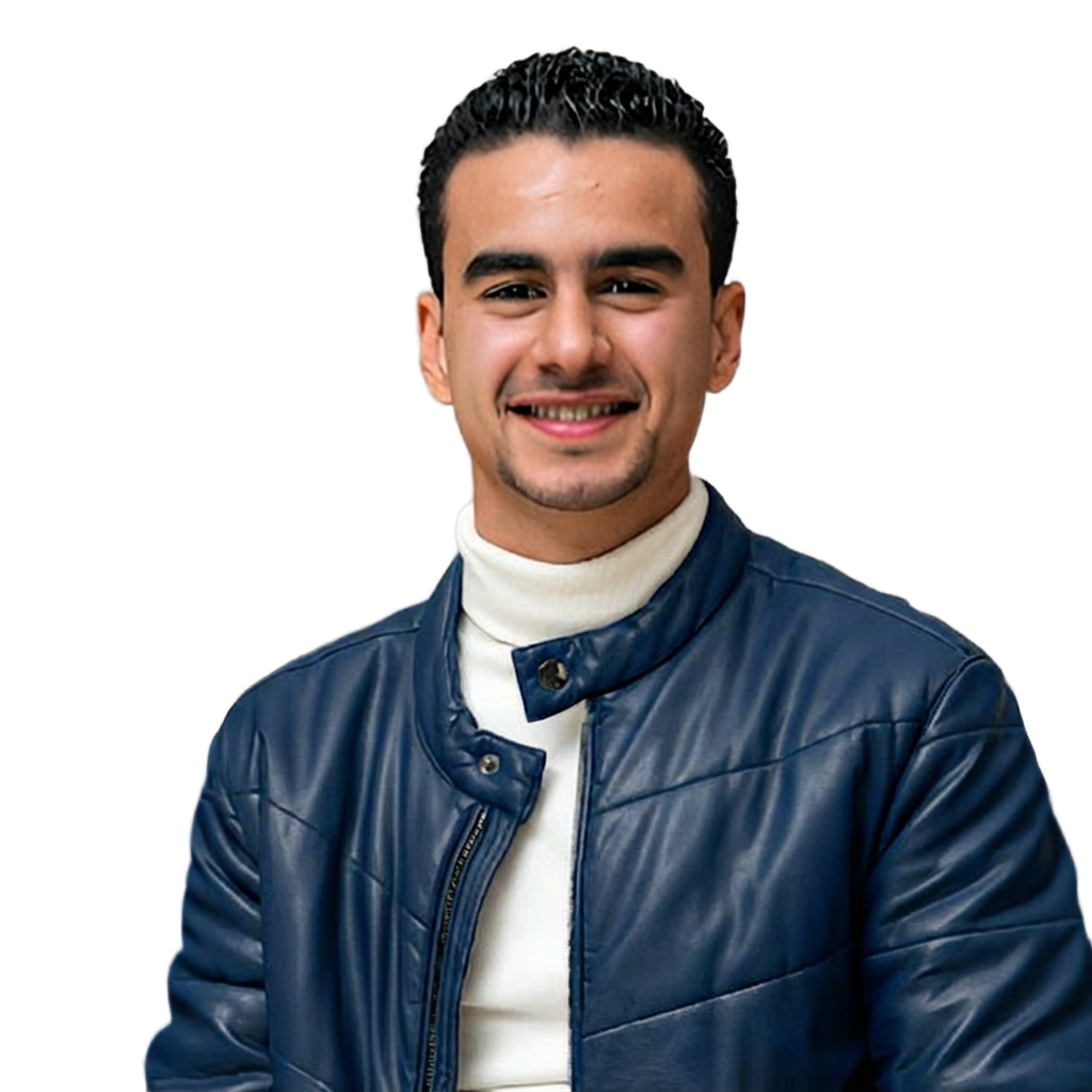 Un jeune homme souriant porte une veste en cuir bleu et un col roulé blanc, assis devant une table avec une nappe rouge et un fond neutre. Il a les cheveux frisés et une barbe légère.